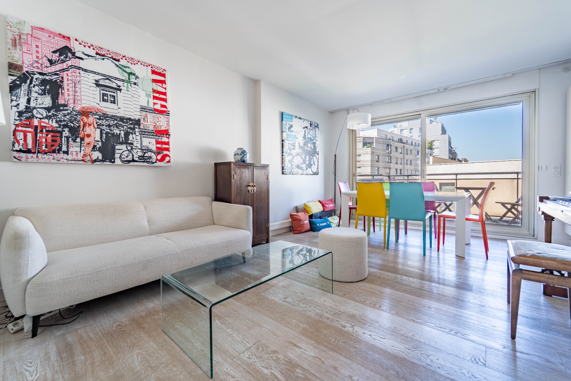 Séjour lumineux avec canapé beige, table basse en verre et chaises colorées