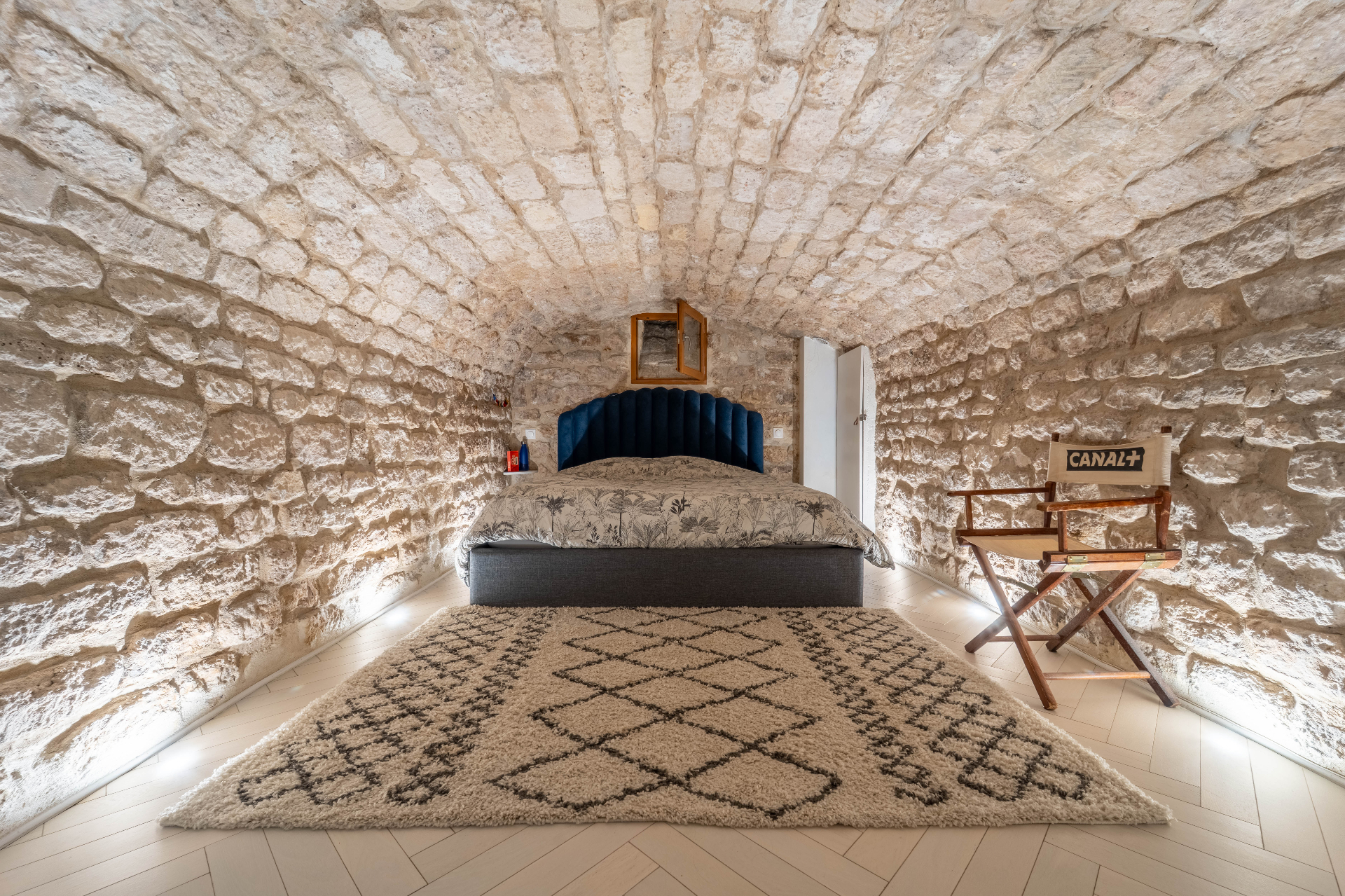 Chambre voûtée en pierres apparentes avec tête de lit velours bleu et tapis berbère